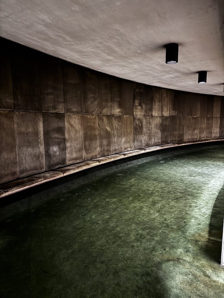 A circular wall with brown bench seating and green carpet underneath. 