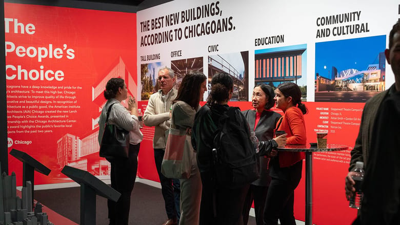 A group of people standing around in an exhibit space and chatting.